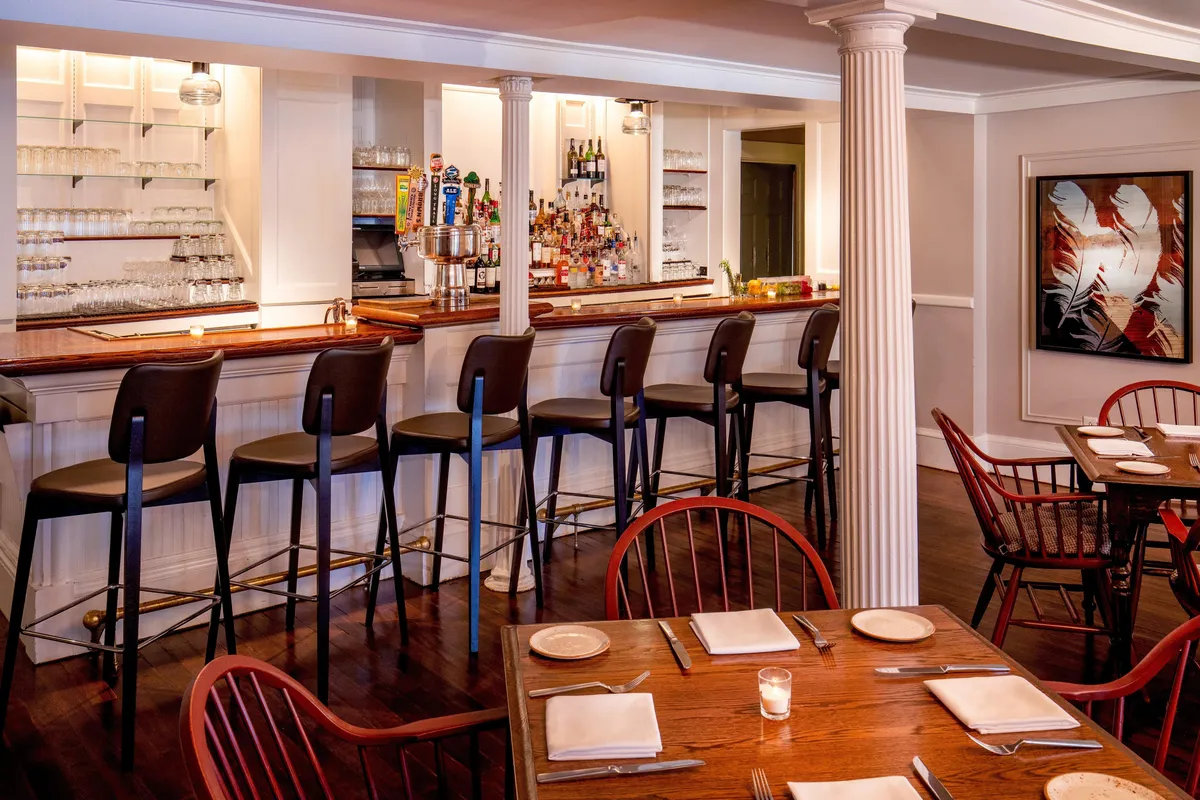 An inviting interior bar area with a polished wooden counter, stylish stools, and tasteful wall art. The vibrant, social setting is ideal for mingling after a day of fitness, wellness, or leisure activities.