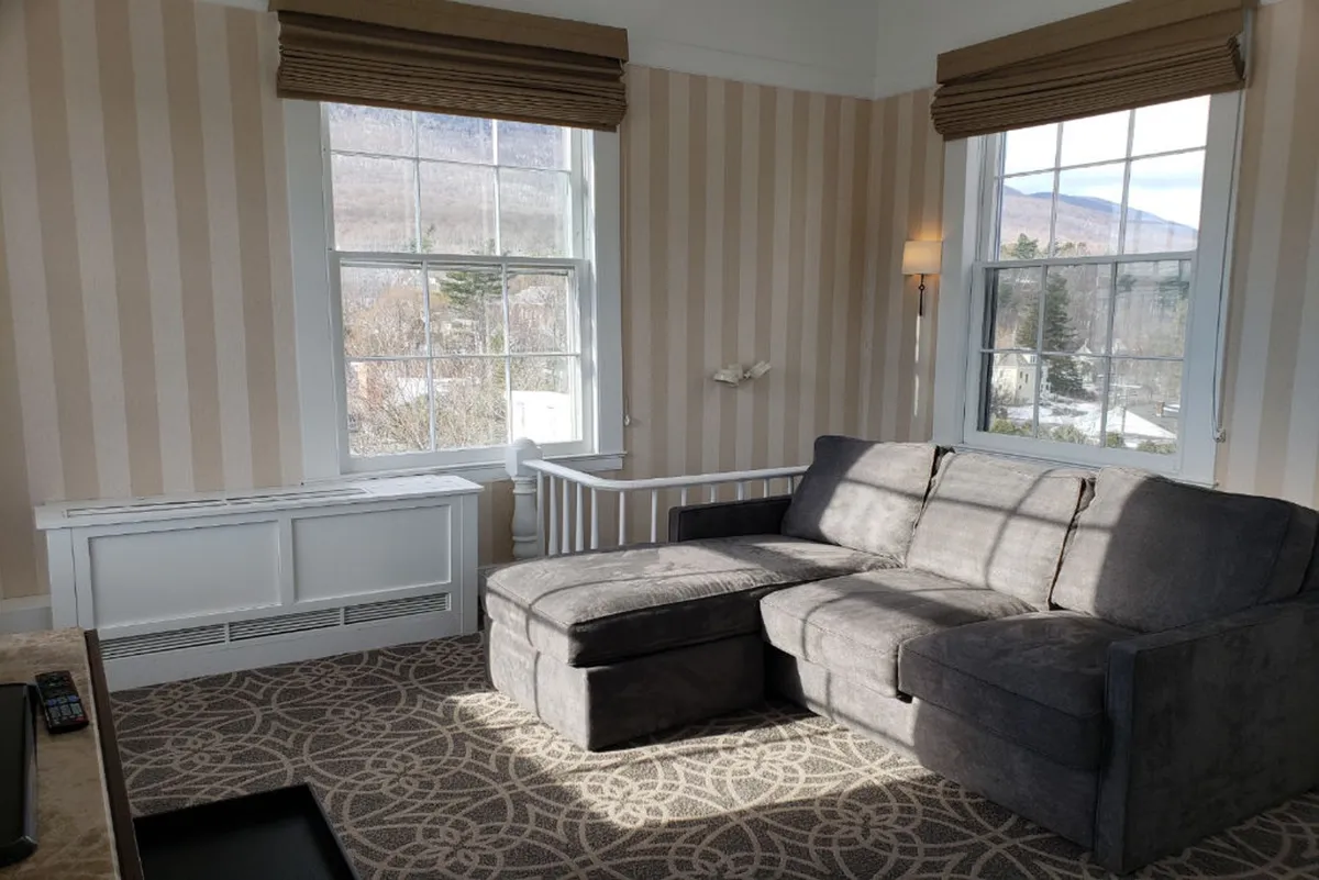 A comfortable, sunlit interior space with a gray sectional sofa, large windows, and striped wallpaper. The room exudes a relaxed, welcoming atmosphere, suitable for unwinding after wellness activities or connecting with Wi-Fi for business or leisure.