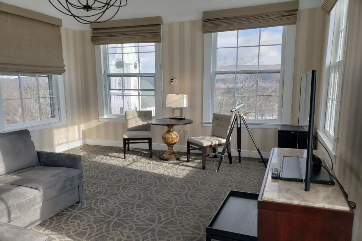 This inviting living area showcases a plush sofa, a decorative table with a lamp, and a telescope positioned beside expansive windows. Natural light floods the space, inviting relaxation or stargazing, while the telescope hints at the cupola's unique panoramic views.