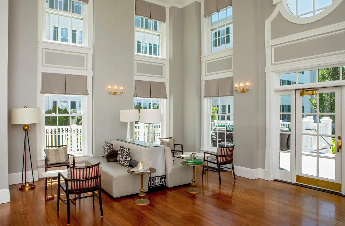 A sunlit, comfortable seating area featuring a stylish lamp, elegant side table, and large windows. The arrangement invites socializing, reading, or quiet moments as sunlight streams in, exemplifying the suite's spacious, welcoming atmosphere.
