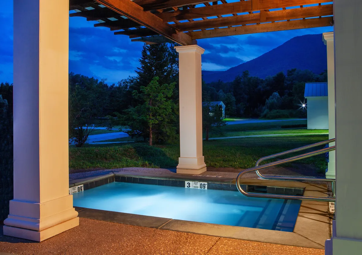 This image presents a serene resort pool area, framed by a stylish pergola, with panoramic mountain views and verdant greenery in the background. The mood is calm and intimate, hinting at leisurely swims, peaceful evenings, and opportunities for stargazing or sharing a sunset toast.
