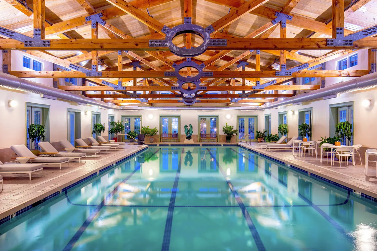 This image showcases a calm, sunlit indoor pool area with elegant wooden beams, lounge chairs, and plant arrangements. The inviting space emphasizes both relaxation and recreation, capturing the essence of a heated indoor lap pool as described in the section.